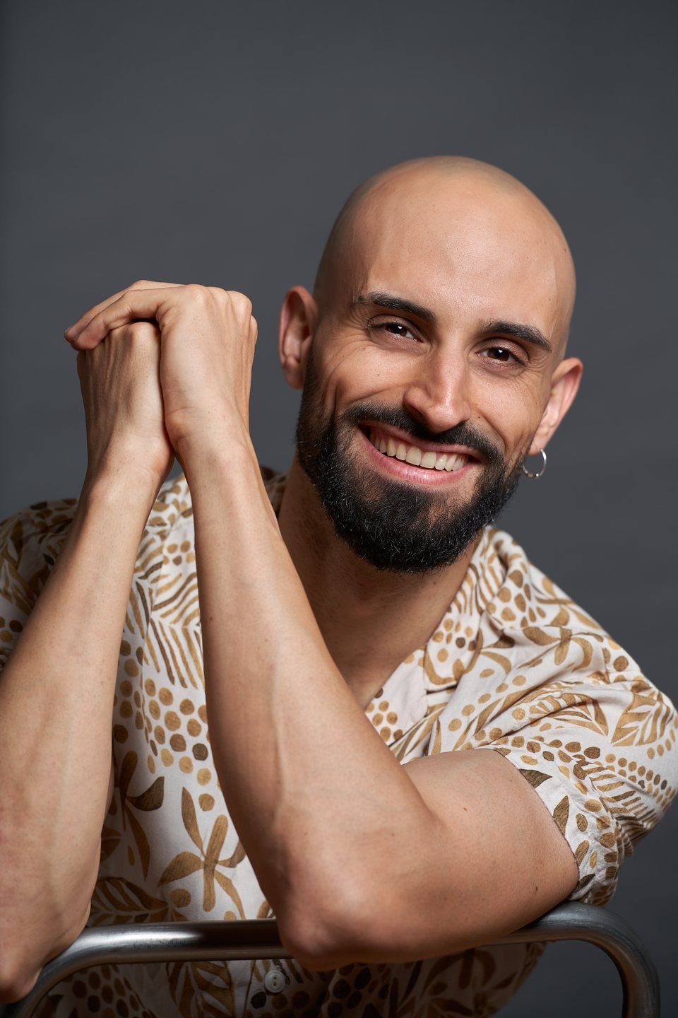 Sonriendo, apoyado en el respaldo de una silla, con camisa estampada
